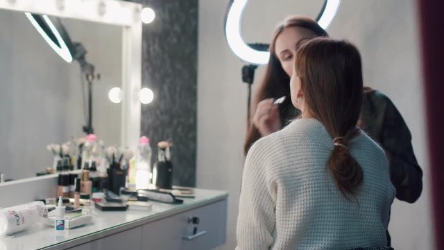 A stylist doing makeup beautiful woman in studio