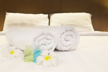 Hotel towel with flower and shampoo and soap bottle set on white bed