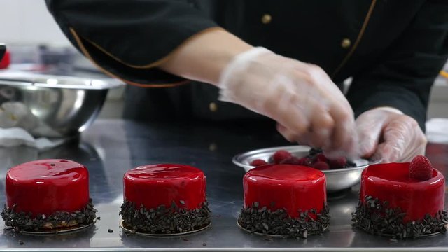 A professional confectioner decorating several mono portions with raspberries and blackberries...