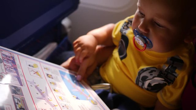 Baby in airplane points to drawings in flight safety instructions. Close up shot