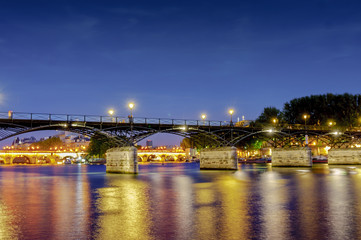 Fototapeta na wymiar Love Bridge called Pont des Arts on a famous beautiful La Seine river in Paris, France. Best tourists destination in Europe. Taken by long exposure by night photography. Landmark in Paris and historic
