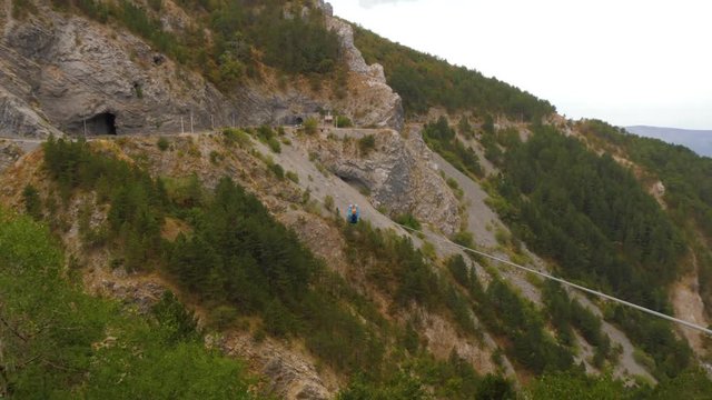 Zip-line in mountains. Man helps a woman to lounch pushing her for higher speed
