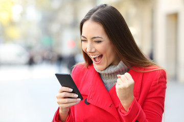 Excited woman winning on line on the street in winter