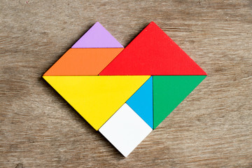 Colorful tangram puzzle in heart shape on wood background