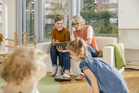 Pre-school teachers with tablet looking at children in kindergarten