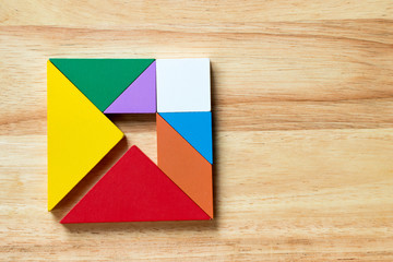 Color tangram puzzle in square with arrow inside shape on wood background