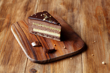 Piece of layered Chocolate Hazelnut Mousse Cake covered with chocolate glaze and decorated with chocolate elements, on wooden board, on wooden background.