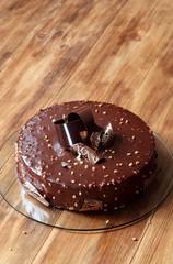 Chocolate Hazelnut Mousse Cake covered with chocolate glaze and decorated with chocolate elements, on wooden background.