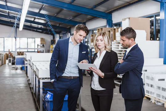 Three business people discussing on shop floor, using digital tablet