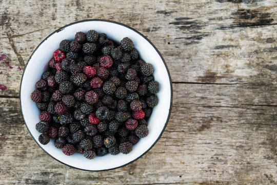 Ripe blackberries in rustic bowl on old wooden background. Top view