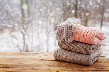 Stack of knitted clothes on wooden tableon winter nature background.