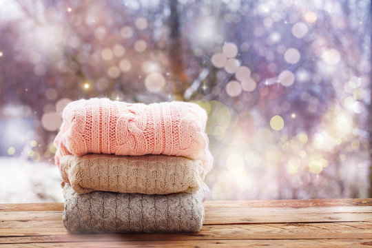 Stack of knitted clothes on wooden tableon winter nature background.