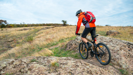 Fototapeta premium Cyclist in Red Riding the Mountain Bike on Autumn Rocky Trail. Extreme Sport and Enduro Biking Concept.