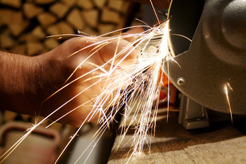 The sparks fly while men's hands grind the metal part on the grinding machine at the factory