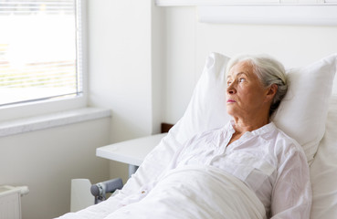 sad senior woman lying on bed at hospital ward