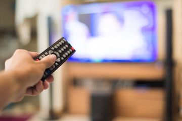 Hand holding use remote control and watching television at home