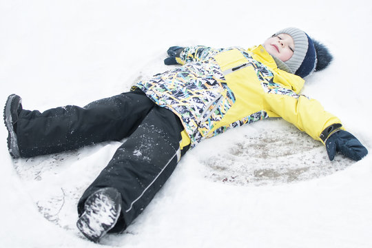 A child, a boy, lies on the snow, makes a snow angel with his arms and legs, emotions, laughs