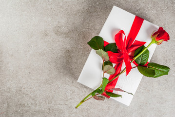 Holiday  background, Valentine's day. Wrapped gift box with one red rose. On a gray stone table, copy space top view