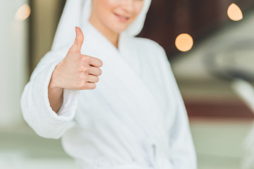 cropped shot of woman in bathrobe at spa salon showing thumb up