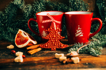 Close-up two glass cups full of hot, red, aromatic lemon tea with dark chocolate on a pine branch and table background. Winter snacks composition.