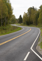 Fototapeta na wymiar Curvy asphalt road on autumn day in Finland. Yellow lines and clean road. Highway to drive.