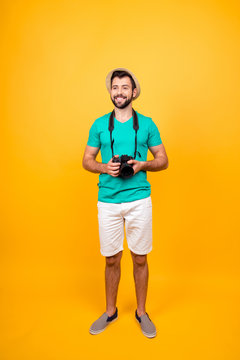 I want more adventures! Vertical full-length portrait of happy positive cheerful joyful handsome tourist with digital camera, wearing shorts and tshirt, isolated on vivid yellow background