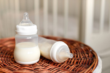 Bottles with milk for baby on a straw basket. Kids room with a bed.