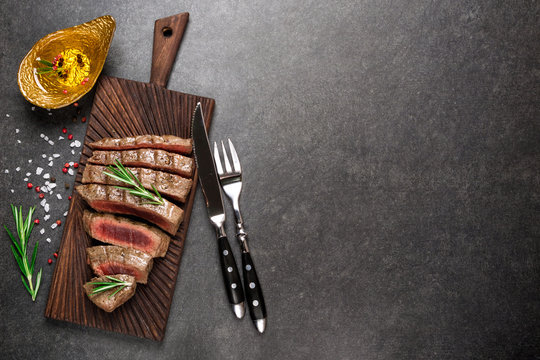 Grilled beef steak on cutting board with rosemary and spices. Rare steak top view, copy space