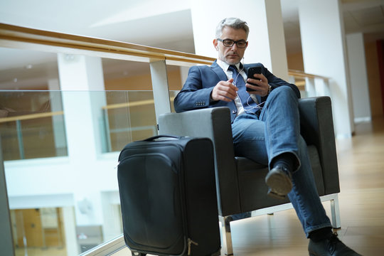Businessman in airport waiting area connected with smartphone
