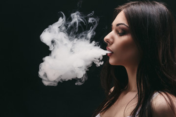 Young woman vaping e-cigarette with smoke on black