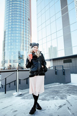 Street style. Winter portrait to the utmost the young attractive girl with a coffee glass in a hand in the urban environment. 