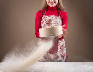 Young woman having fun with flour while making dough. Sifting flour with flour filter. Womans hands sifting bread-stuffs through a sieve for baking. Chef's Hands Sifting Flour. Chef preparing dough.