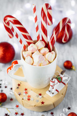 Cup of hot cocoa with marshmallows and candy canes on blue rustic background with Christmas lights of bokeh