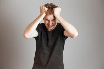 Portrait of angry rage redheads man touching his hair clenched teeth. Over grey background. Copy...