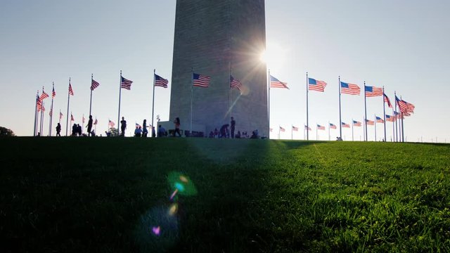 People are resting near the Washington Monument in the very center of the American capital. The sun shines because of the obelisk