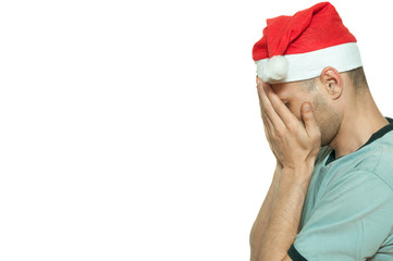 Young man with Santa Claus hat cover his face with his hands feeling lonely and sad for New Year and Christmas holiday depression concept