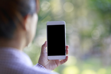 Hand holding smartphone with bokeh of trees