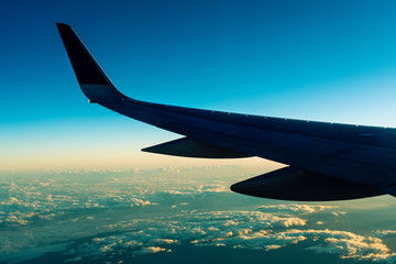Fototapeta premium Beautiful sunset with wing of airplane with beautiful cloud and blue sky in background. Airplane wing and blue sky with copyspace for text.