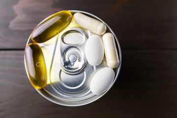 Complex of vitamins and dietary supplement, yellow capsules of omega 3, white capsules of glucosamine, calcium pills on the aluminum beverage can, at wooden table, top view