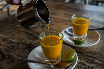 Adding honey to two healthy jamu shots in close-up.