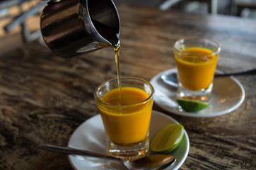 Adding honey to two healthy jamu shots in close-up without hand.