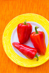 three red peppers on a colorful plate closeup.