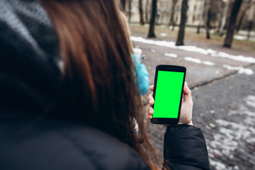 stylish hipster traveler woman holding phone with empty screen in city street. smartphone in girl hand in winter