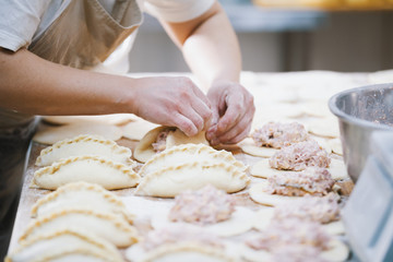 Cook is shaping meat pies by hands in the bakery