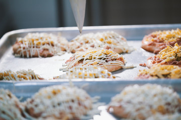 Cook puts the sauce on the mini pizza in the bakery
