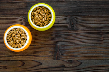 Dry pet food in bowls on dark wooden background top view copyspace