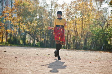 Fototapeta premium African american girl at yellow and red dress at golden autumn fall park.