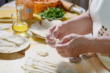 The hands of an elderly woman prepare a pie of thin fresh dough with stuffed minced meat and spicy...