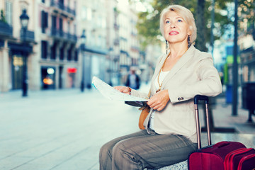 Mature female tourist is sitting with map