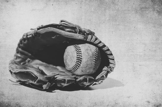 Vintage style grunge image of baseball in glove, shows sport equipment for game.  Ball caught in mitt in black and white.